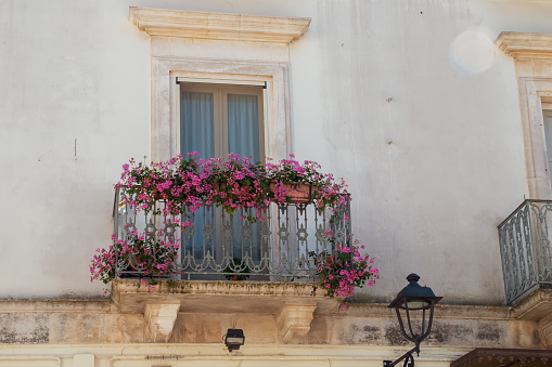 A balcony of a traditional house with pots of pink flowering geraniums to beautify the facade.