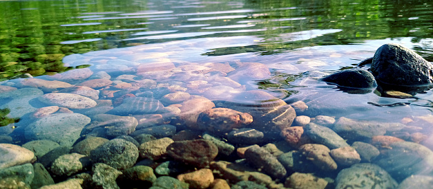 the clear surface of the river water reflects light from the sky against a background of colorful pebbles under the water