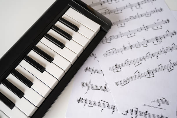 istock Selective focus of home synthesizer with sheet music (musical) notes on a white table. Piano keyboard. 1456550394