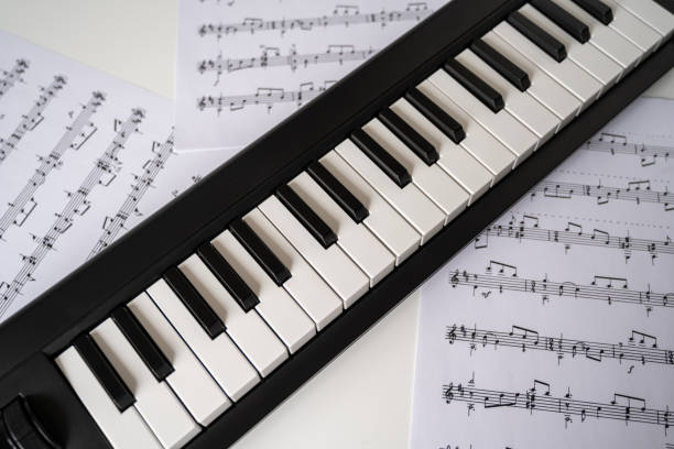 Selective focus of home synthesizer with sheet music (musical) notes on a white table. Piano keyboard.