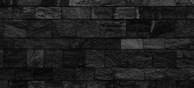 Dark and scary black stone wall background. Panoramic view of a wide empty old black block stone wall texture
