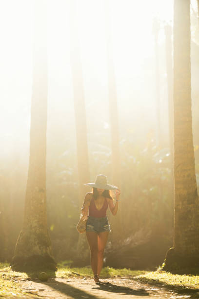 silhouette d’une belle fille portant un grand chapeau et un bikini rouge marchant sur un sentier entouré de cocotiers lors d’un magnifique coucher de soleil. île de siargao, philippines. - people traveling elegance philippines palawan photos et images de collection