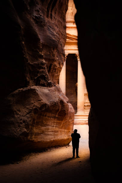 silueta de un turista frente al hermoso al khazneh (el tesoro) visto a través de las paredes de un cañón en petra. petra es una ciudad histórica y arqueológica en el sur de jordania. - siq al barid fotografías e imágenes de stock