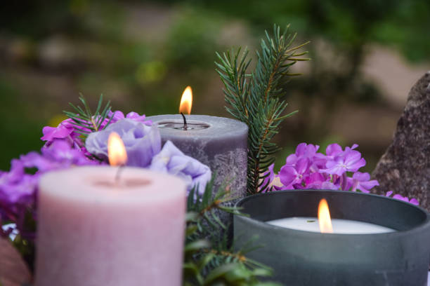Closeup burning candles purple flowers stone on blurred background Closeup burning candles purple flowers stone on blurred background. Selective focus on light candlewick. Beautiful composition with violet candles for spa treatment. Zen relax memorial concept. pink memorial candle with flowers stock pictures, royalty-free photos & images
