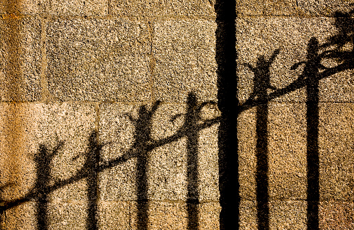 Shadow of carved cast iron railing on stone wall background. Close-up full frame view suitable for background. Betanzos, A Coruña province, Galicia, Spain.