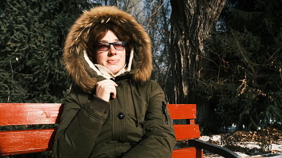 Portrait of mature woman sitting on the bench in sunny winter park