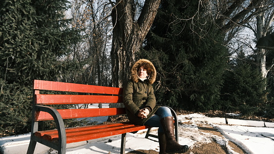 Portrait of mature woman sitting on the bench in sunny winter park