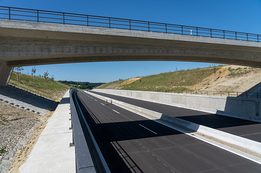A concrete bridge spans the six lanes of the newly built motorway A94 between the Bavarian cities of  Munich and Passau. The motorway is not open for cars and two cyclists riding their bike on the tarred surface.