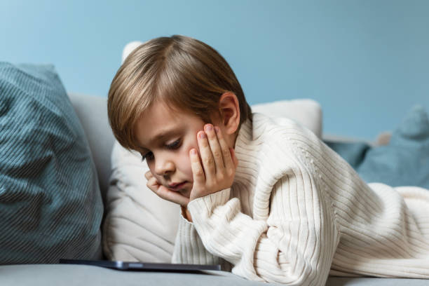 istock Boy spends time behind a screen on a tablet on the sofa in the living room. Digital device. Technologies. 1456560375