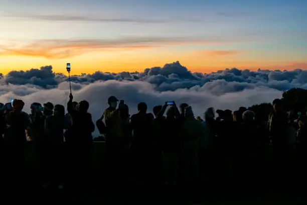 Silhouette person group watching floating sea of clouds,Sea of fog, Sky above clouds,taking cloudscape photos with mobile phones in the morning,sun rising,travel long weekend,Inthanon mountain.