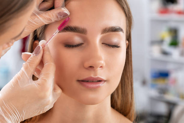 The make-up artist does Long-lasting styling of the eyebrows of the eyebrows and will color the eyebrows. Eyebrow lamination. Professional make-up and face care. stock photo
