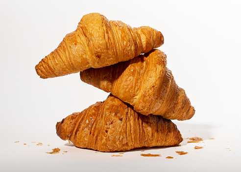 Three stacked fresh croissants, French bakery, sweet dough dessert composition with crumbs. High quality photo