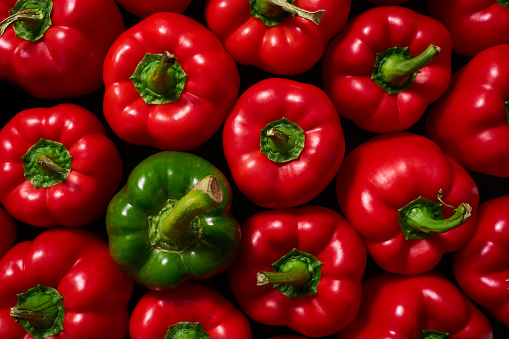 A single green sweet pepper surrounded by a group of red peppers. Sweet green and red bell peppers, top view.
