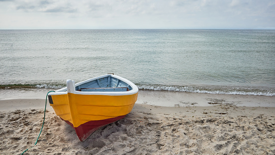 A panoramic view of a tropical ocean with boats scattered throughout. The ocean is a beautiful turquoise color and the sky is blue with white fluffy clouds. The boats are different colors and sizes, some are closer to the shore and some are further out. The shore is sandy and there are trees and buildings in the background. The photo is taken from a high vantage point and the horizon is visible.