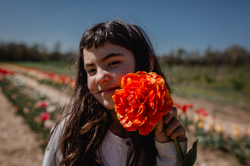 portrait of girl with dark hair holding big orange tulip in colorful flower field