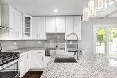 A white kitchen with a stainless steel apron sink, granite countertops and white cabinets.