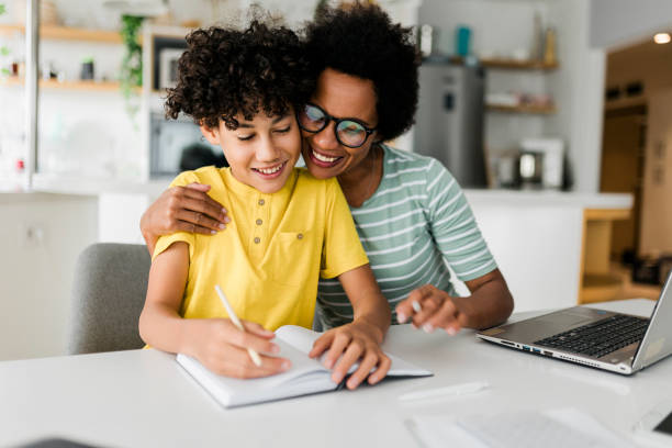 istock Boy writing on a book while his mother working on laptop. Kid studying with mother working from home. 1456573514