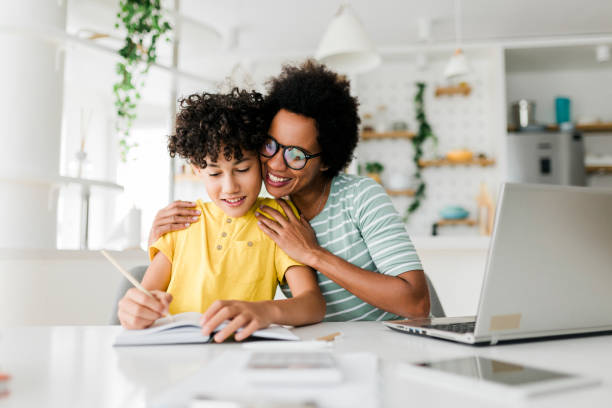 istock Boy writing on a book while his mother working on laptop. Kid studying with mother working from home. 1456573524