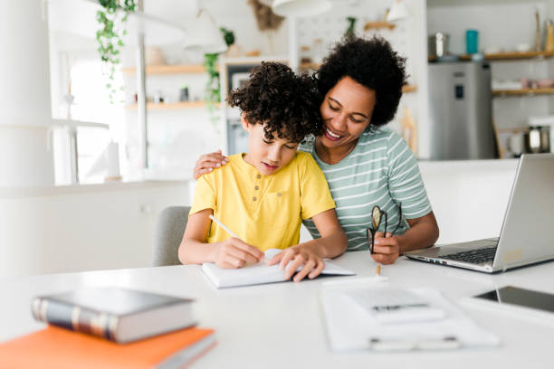 istock Boy writing on a book while his mother working on laptop. Kid studying with mother working from home. 1456573535