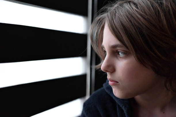 istock Sad stressed teenage boy watching at the window with blinds 1456577177