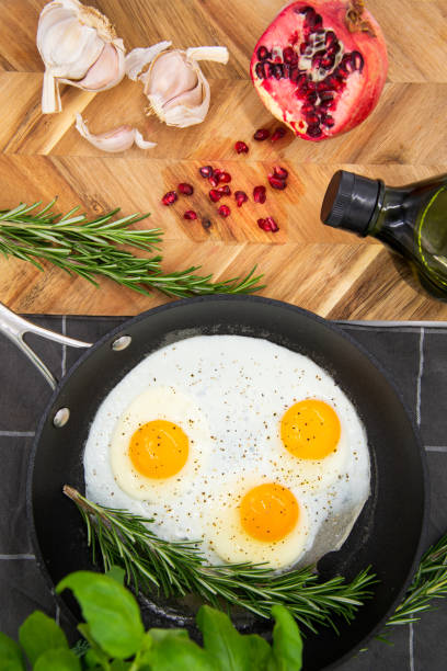 breakfast or brunch, fried eggs in black pans and red pomegranate with garlic and basil. view from the top.