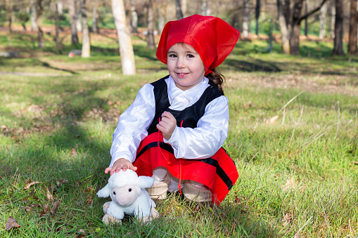 Caucasian little girl dressed as a shepherdess with a stuffed sheep.  Caucasian shepherd girl looking at camera.  Girl in a shepherdess costume.