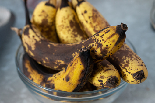 a close up of a bunch of yellow-brown bananas sitting in a glass bowl on a marbled countertop