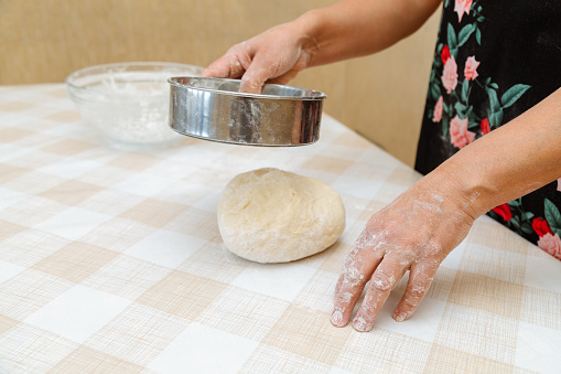 Closeup of woman sifting flour with sieve over dough on table