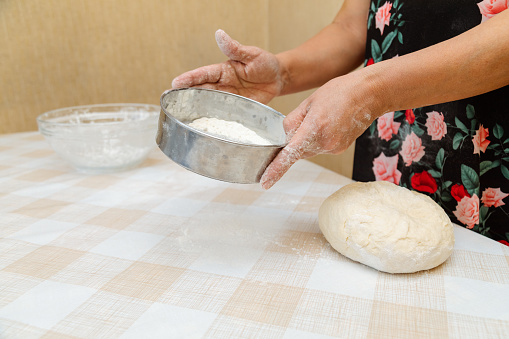 Closeup of woman sifting flour with sieve over dough on table
