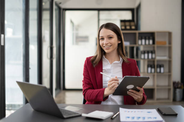 istock Beauty business woman using her digital tablet while sitting on a desk in a modern startup office. 1456587341