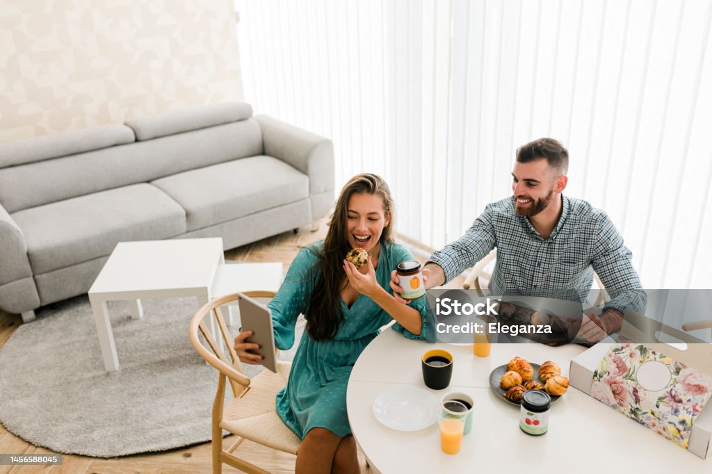 Happy couple using digital tablet while enjoying breakfast together Adult Stock Photo