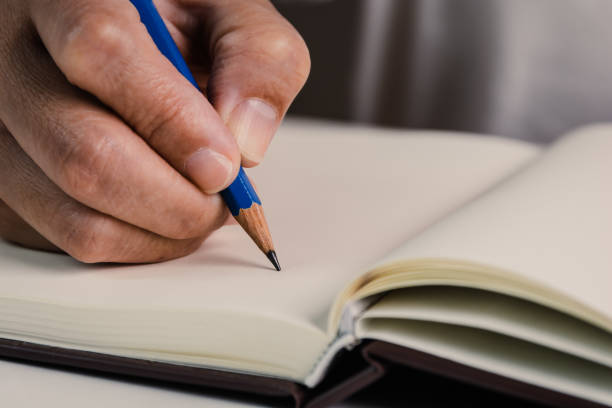 istock Close up image of pencil in people's hand start writing down something in the empty open book for study, learning, idea concept. 1456588381