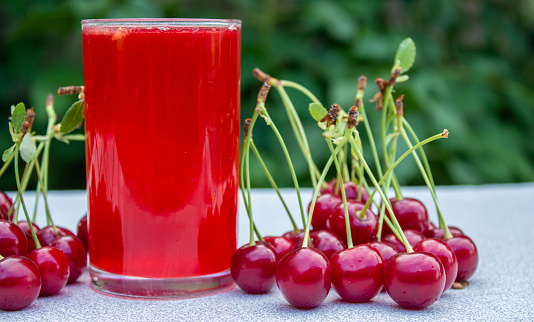 A glass of cherry juice on wooden table with sour cherry fruits. Homemade juice.