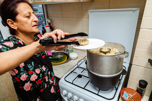 Woman checking the readiness on cooking manti (dumplings) with tongs on a stove