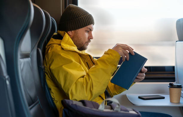 istock Man in winter yellow jacket and hat reading book while traveling by train sitting inside train. 1456593325
