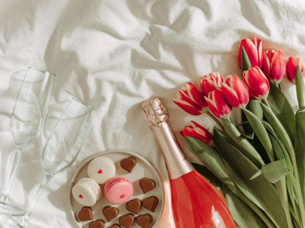 Bunch of red tulip and rose wine on bed sheets stock photo