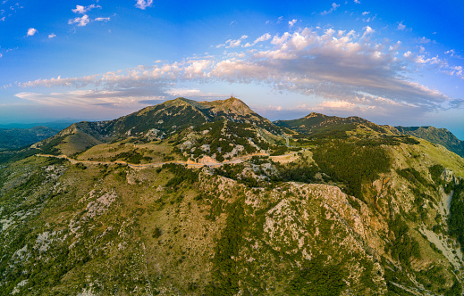 Panorama of peaks of the Montenegrin mountain massif Durmitor with slopes covered with mountainous green vegetation and pedestrian winding tourist paths against the background of evening cloudy sky