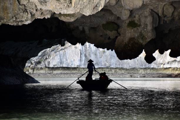 Silhouette of Vietnamese Woman Rowing Boat through Sea Cave stock photo