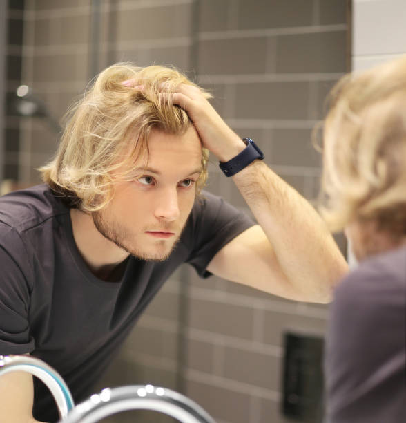 istock young man looking in the mirror,combing his hair,looking at problems on face 1456598587