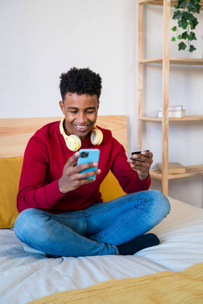 istock Black man with smartphone sitting on bed shopping online 1456599081