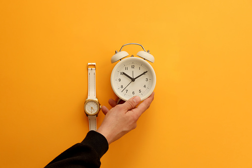 Woman holding alarm clock with analog watches on orange background