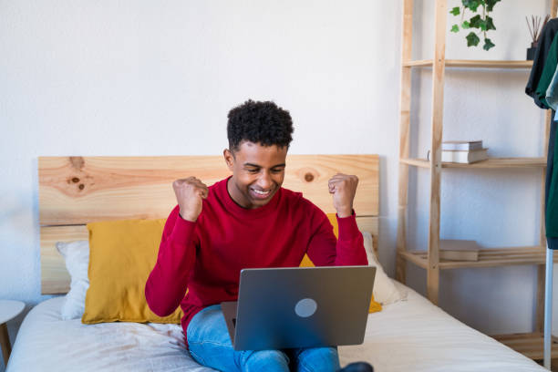 istock Cheerful black man using laptop on bed celebrating some good news 1456599966