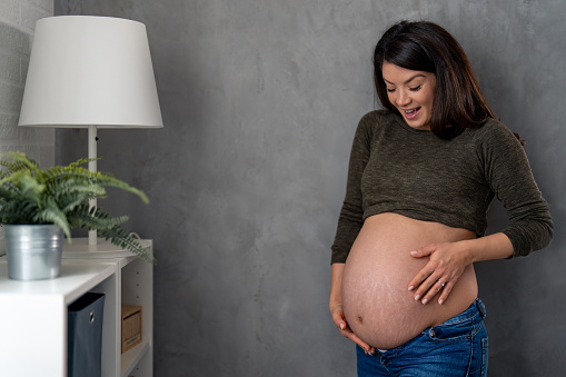 Beautiful pregnant woman with excitement on her face feeling how her baby moves in stomach.