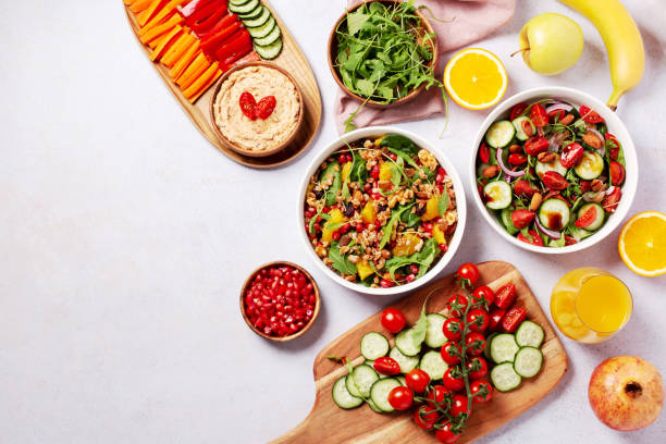 さまざまなサラダとライトグレーのテーブルの上の健康的なプレートを備えたビーガンまたはビーガニュアリーのごちそう - nut directly above multi colored food ストックフォトと画像