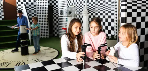 Photo of Tween girls solving conundrum in quest room stylized under chessboard