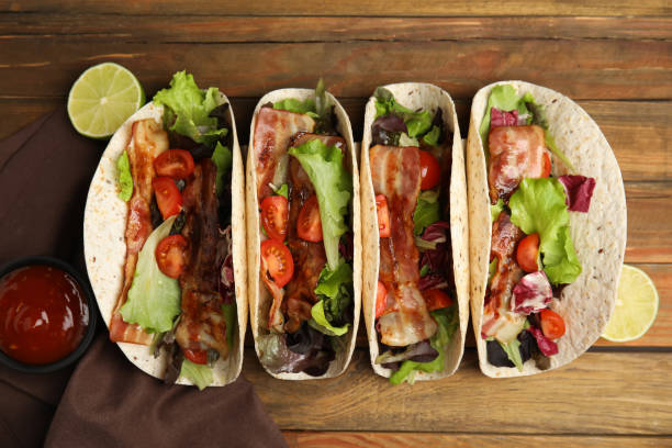 istock Delicious tacos with fried bacon and lime on wooden table, flat lay 1456606650