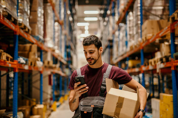 Warehouse worker texting on phone stock photo