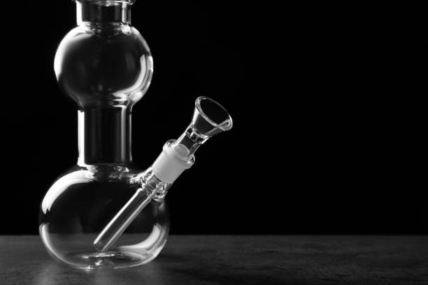 istock Glass bong on grey table against black background, space for text. Smoking device 1456607033