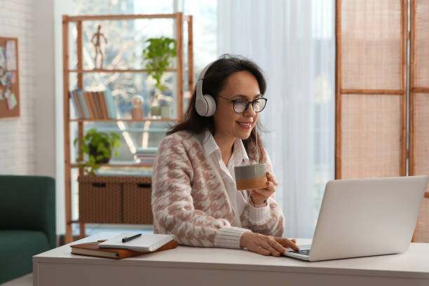 istock Woman with modern laptop and headphones drinking tea while learning at table indoors 1456609882