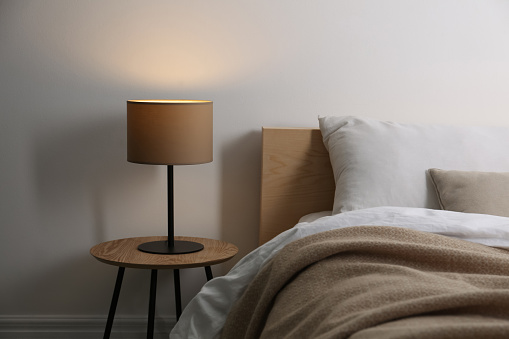 Stylish lamp on table near bed indoors